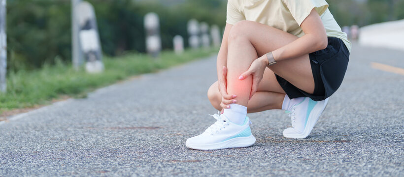 Young adult woman runner suffering from acute calf muscle pull and leg ache during running workout. female athlete holding his painful leg due to sports injuries. Medical and healthcare concept
