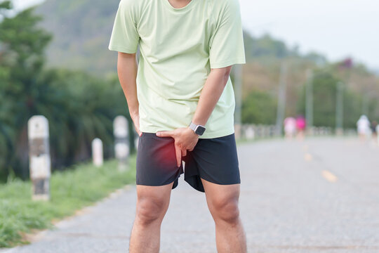 Young adult male runner suffering from acute groin pull and muscle pain during running workout. Man holding his inner thigh due to sports injury and strain. Medical and healthcare concept