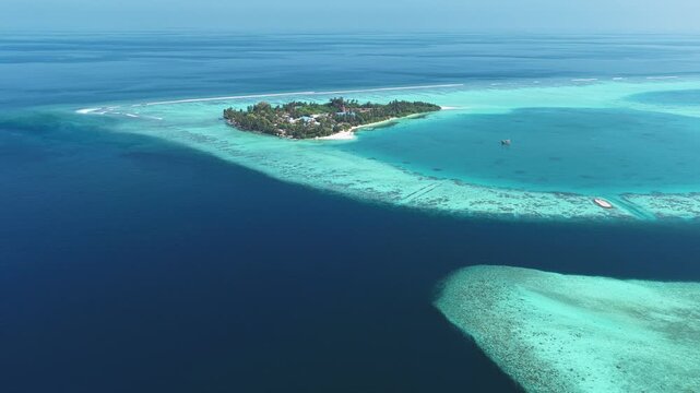 Aerial view of a lush tropical island surrounded by turquoise coral reefs and deep blue ocean waters in Kudahuvadhoo, Dhaalu Atoll, Maldives.