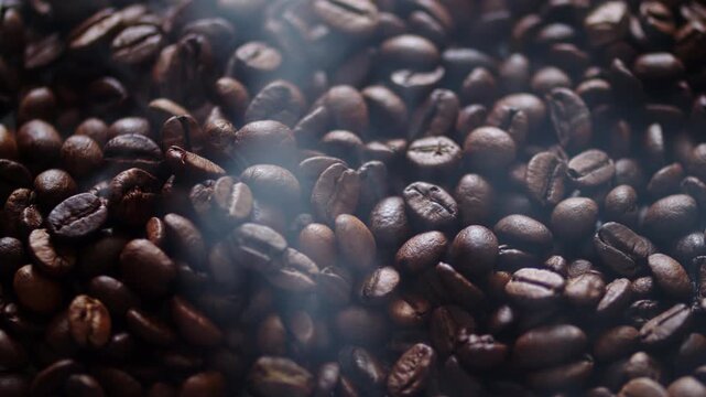 Freshly roasted brown coffee beans with hot smoke rising from them. Warm aromatic arabica coffee beans smoking after roasting. Coffee production process.