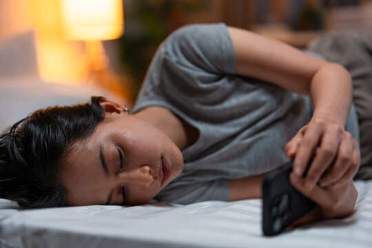 Depressed young Asian woman looking at mobile phone device at night. 