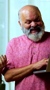 Senior Indian couple holding a five hundred rupee money fan with a laptop, looking surprised and joyful while cash is raining from above to denote sudden growth