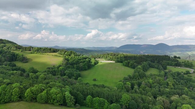 Aerial view of green countryside with rolling hills meadows and forest under cloudy sky in summer in Poland