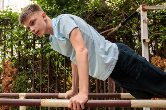 Teenage boy practicing bodyweight fitness routine on outdoor parallel bars, focused adolescent athlete developing strength, coordination and endurance through calisthenics and functional training