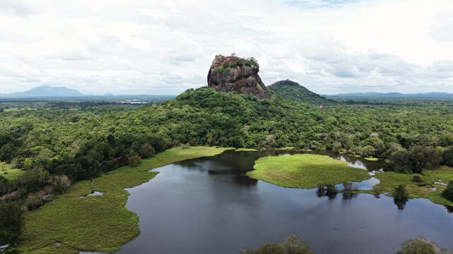 Aerial view of Sigiriya Rock fortress rising above the lush green jungle and a calm lake under a cloudy sky in Sigiriya, Central Province, Sri Lanka.