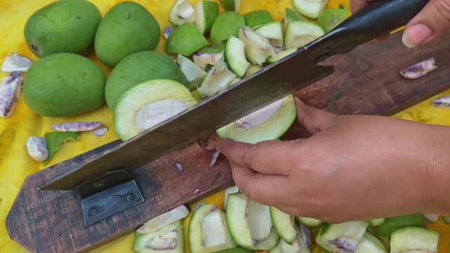 Close view of hands using a traditional Indian manual mango cutter to split raw green mangoes into pieces during homemade pickle preparation in a rural kitchen setting
