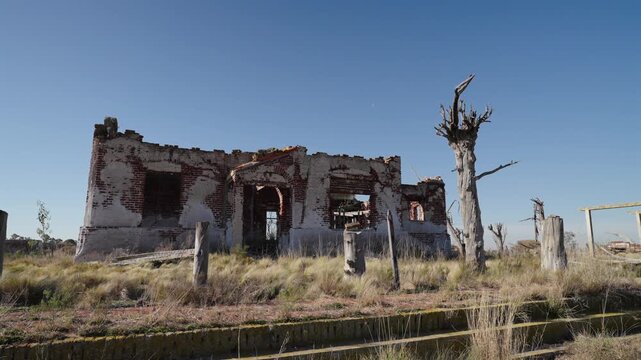 Static right pan of ruined brick building and skeletal dead trees at Villa Epecu&eacute;n under a vivid blue afternoon sky.