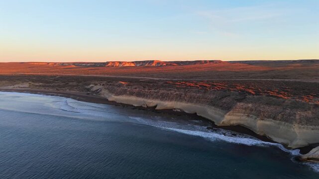 Sunrise over calm ocean waters with soft light along Puerto Madryn coastline in Patagonia, aerial drone overview