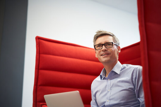 Businessman with laptop in red chair at office