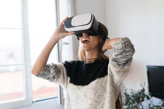 Excited young woman wearing VR glasses at home