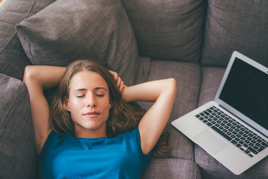 Young woman with laptop lying on couch at home