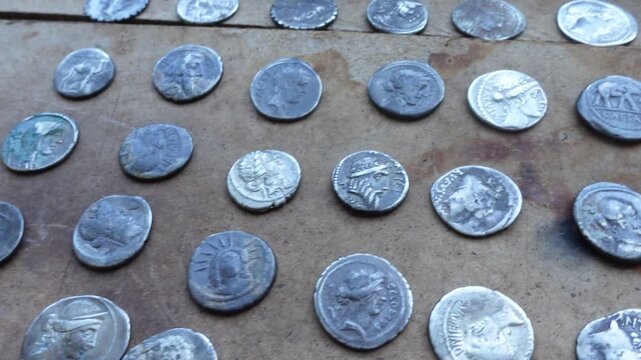 Roman silver coins of various emperors on an antique wooden table.
