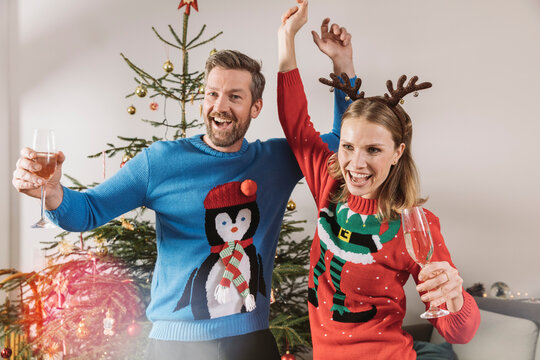 Two people with ugly Christmas sweaters dancing in front of tree
