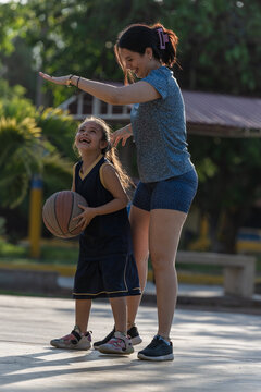 Happy mother and daughter playing basketball outdoors