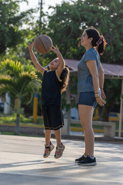 Young girl jumping for a basketball with her mother