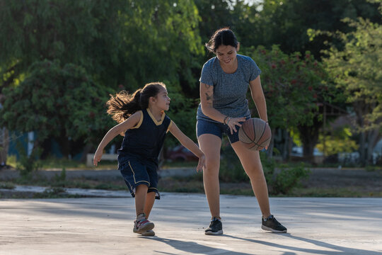 Mother and daughter playing basketball together outdoors