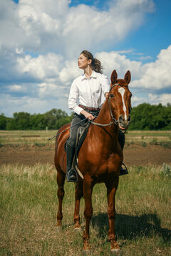 Woman riding a brown horse in a grassy field