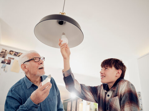 Grandson and grandfather changing old lightbulb for a LED energy saving lightbulb