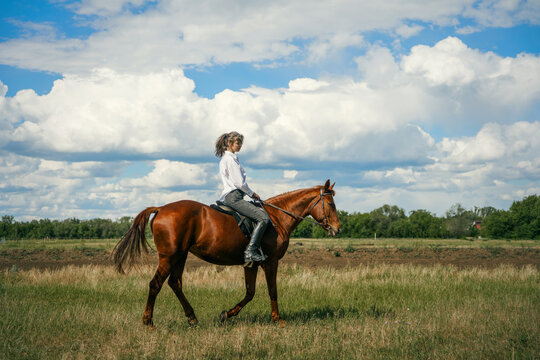 Woman riding a brown horse in a grassy field