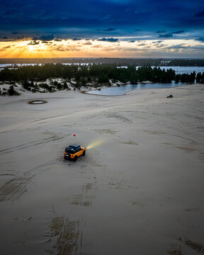 Yellow SUV driving on sand dunes at dramatic sunset
