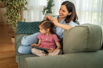 Fototapeta premium Mother styling daughter's hair while bonding on sofa