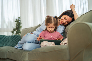 Obraz premium Mother and daughter sitting on sofa using digital tablet