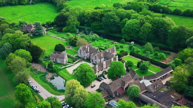 Aerial drone footage of Great Chalfield Manor in Wiltshire, England, showing the historic manor house, chapel, landscaped gardens, pond, outbuildings, trees, and surrounding countryside.