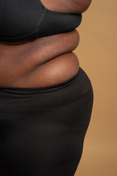 Close-up of belly and back rolls of plus size woman against beige background