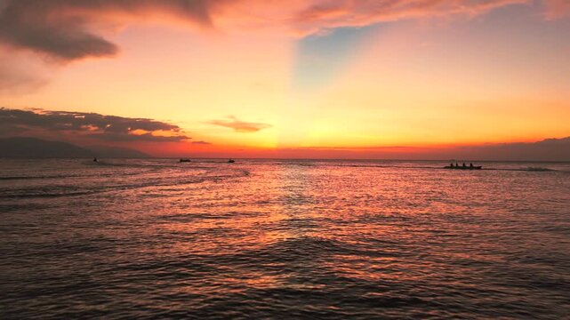 Jet ski and boats crossing tropical ocean during colorful sunset