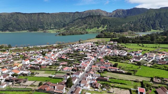 Panoramic drone view of Sete Cidades village on Sao Miguel Island, Azores. Traditional white houses nestled between the volcanic lake shores and lush green mountain craters in PortuGal Europe travel