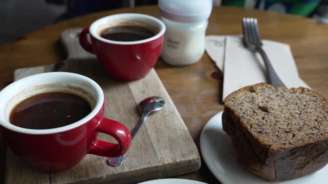 Coffee mugs and banana bread on a wooden board, enjoying a morning break with hot caffeinated beverage in Spain, representing a delicious start to the day