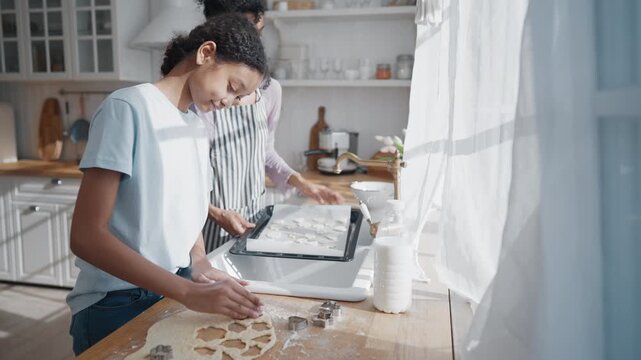 Vertical portrait of happy black teen girl and her mother cooking cookies at home kitchen. Happy family weekend, single african woman and daughter baking tasty homemade sweets for family fest diner,