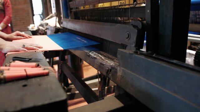 Traditional weaving loom machine producing colorful silk fabric in a vietnamese textile factory with a weaver working
