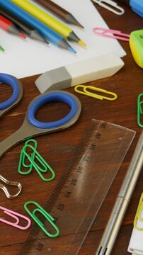 Metal scissors, paperclips, smile binder clips, push pins, pencils, pen, rubber eraser, transparent plastic ruler, white pages of notebook, green sharpener. Workspace filled with stationery essentials