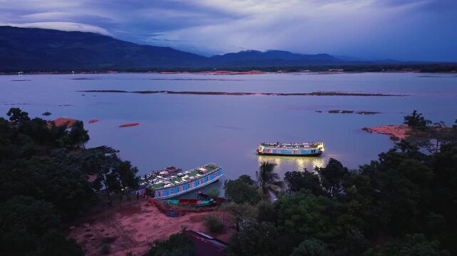 Aerial view of illuminated houseboats on the calm waters of Tanguar Haor at twilight with mountains in the background Sunamganj District, Sylhet Division, Bangladesh.