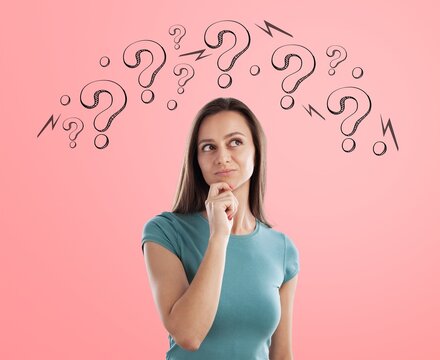 Young woman thinking with question marks above head against a pink studio background