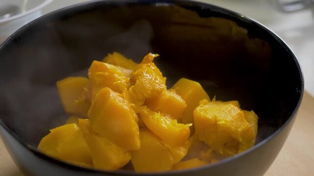 Hot pumpkin slices rest in black dish. Steam reveals warmth of autumn cooking. Halloween celebration marked by natural flavors and harvest food shared in cozy indoor setting