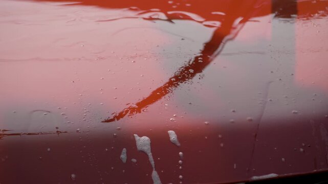 Red car hood covered in foam and grime from regular use. Clean water rinses away residue, restoring smooth surface. Represents effort in maintaining vibrant and polished exterior
