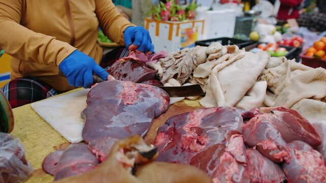 Woman cutting raw meat and liver with a cleaver at a traditional vietnam street market in Ha noi, vietnam