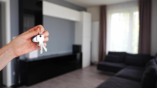 Hand holding apartment keys in furnished resale apartment living room interior. Secondary housing purchase and existing property ownership concept