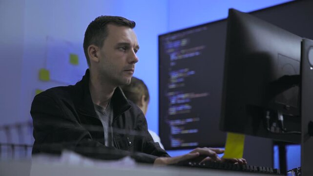Thoughtful male software developer working with colleague in tech office