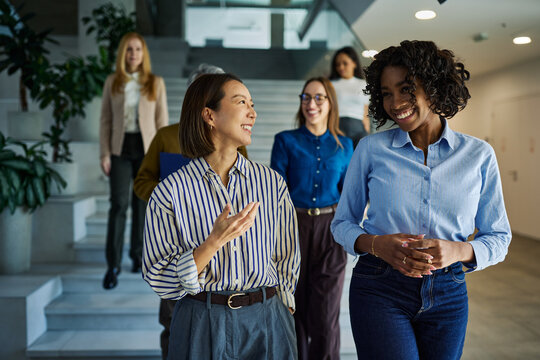Diverse businesswomen walking and talking in office hallway
