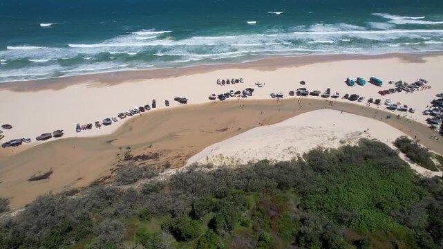 Aerial view of Eli Creek flowing into the ocean with 4WD vehicles parked on the white sand and people enjoying the water K'gari, Queensland, Australia.