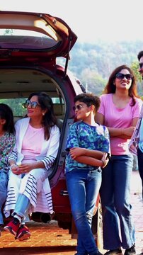 Indian family sitting in car dicky outdoors ready to go for picnic enjoying fun moments, grandparents, parents, and kids relaxing together, sharing laughter and bonding during a joyful outdoor break