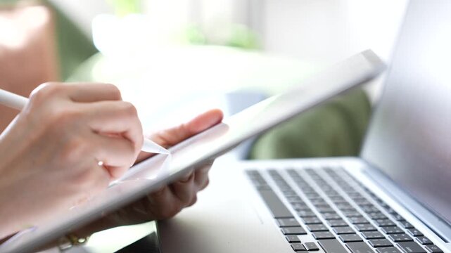 Close up hand confirming customer order on tablet beside laptop. Online business transaction, order management, ecommerce workflow, customer service and digital sales process.
