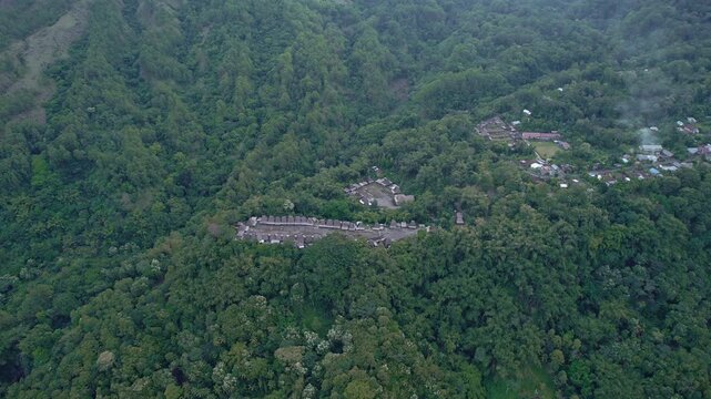 Aerial view of Bena Traditional Village with its iconic thatched roof houses nestled on a lush green mountain slope in Kecamatan Jerebuu, Nusa Tenggara Timur, Indonesia.