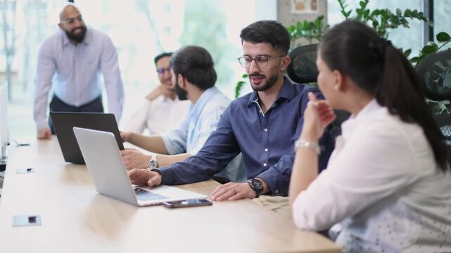 A group of people are sitting around a table with laptops and cell phones