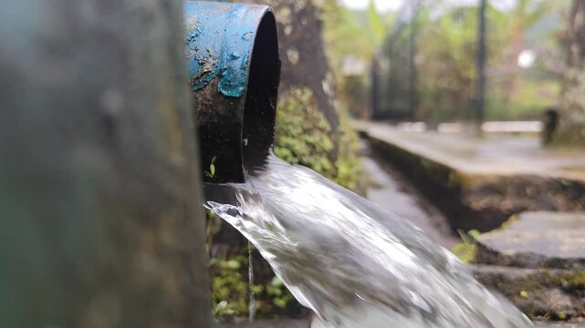 close up of clear water flowing rapidly out of an old blue pipe into a drainage gutter