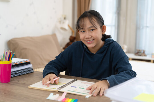 Cheerful young student smiles while completing her schoolwork at a neatly organized study desk at Home
