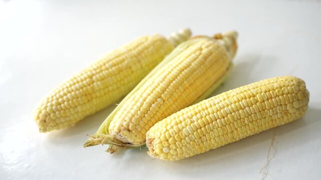 Fresh sweet corn on the cob with partially peeled husks resting on a white surface, highlighting its natural freshness and suitability for healthy cooking and consumption